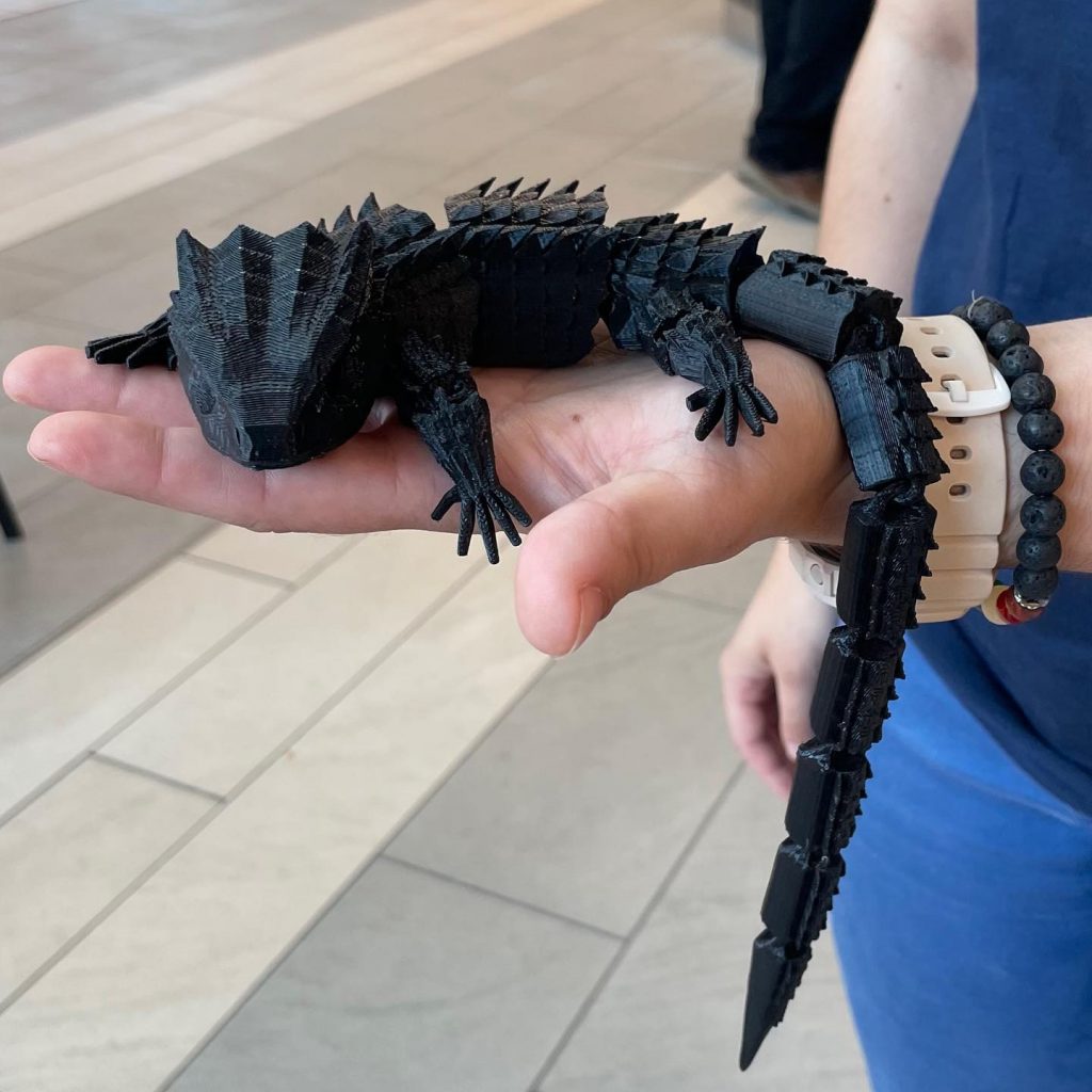 3D print of a lizard, in black, being held by person.